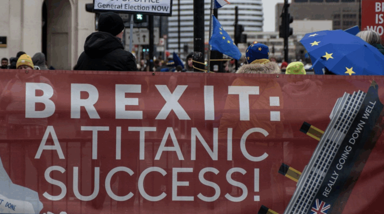 Striscione durante una manifestazione contro la Brexit con la scritta ironica "Brexit: a Titanic success!" e bandiere europee sullo sfondo.