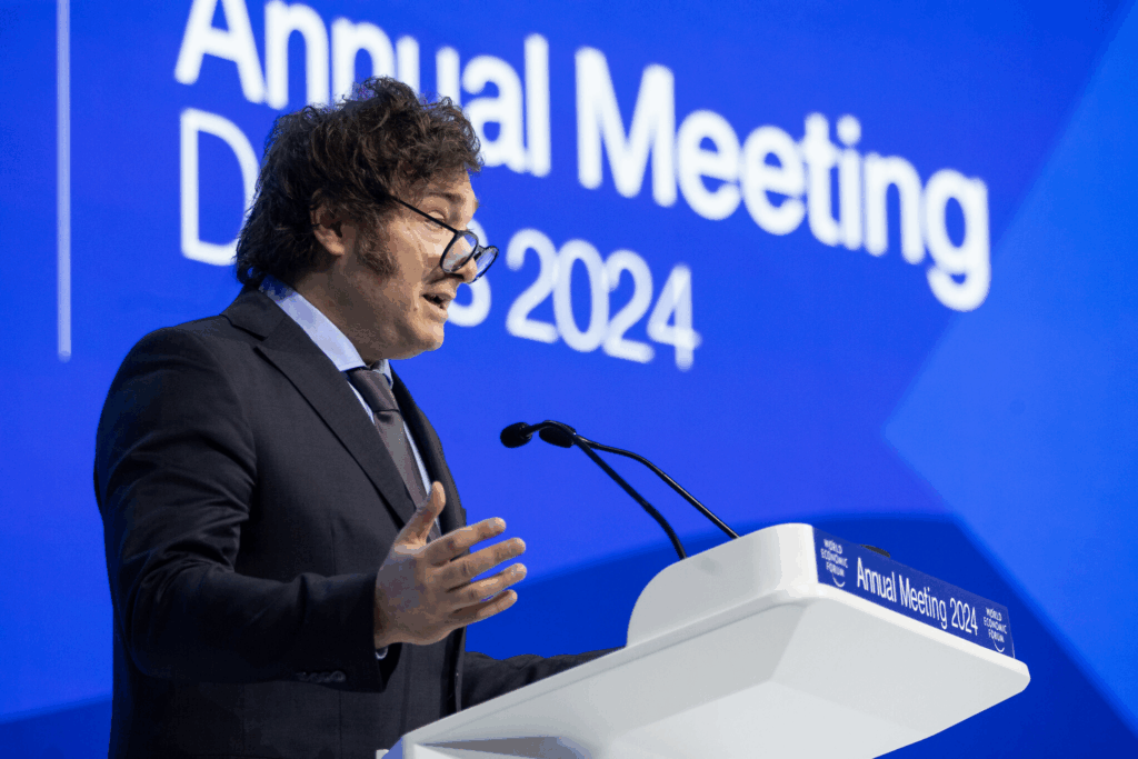 Javier Milei tiene un discorso al podio durante l'Annual Meeting di Davos 2024, davanti a uno sfondo blu con scritta bianca.