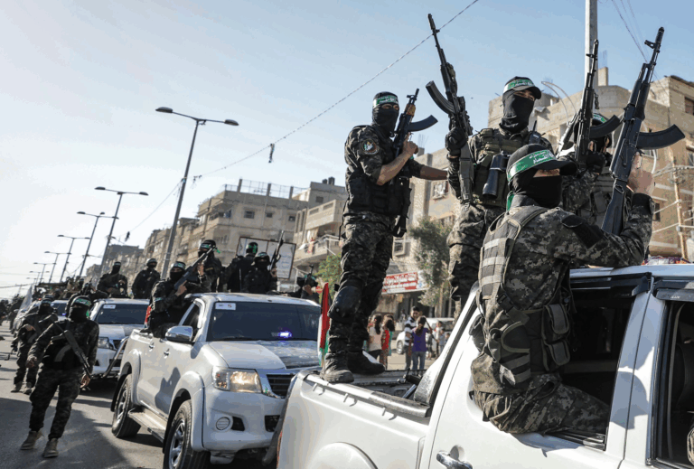Miliziani di Hamas in parata armata su veicoli scoperti a Gaza, tra la folla e le bandiere.