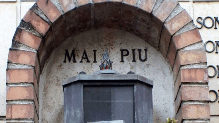 Ingresso di un memoriale con la scritta "MAI PIÙ" scolpita in un arco di mattoni, simbolo del ricordo della Shoah.