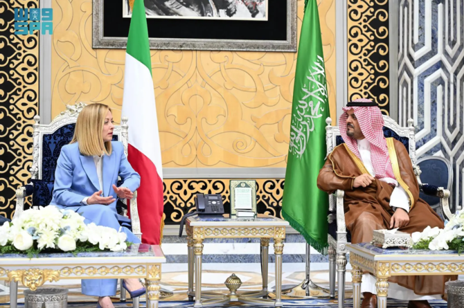 Giorgia Meloni e un rappresentante saudita durante un incontro ufficiale tra Italia e Arabia Saudita, bandiere nazionali sullo sfondo.