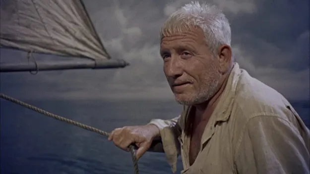 Uomo anziano su una barca a vela, con espressione riflessiva, in mare aperto sotto un cielo nuvoloso.