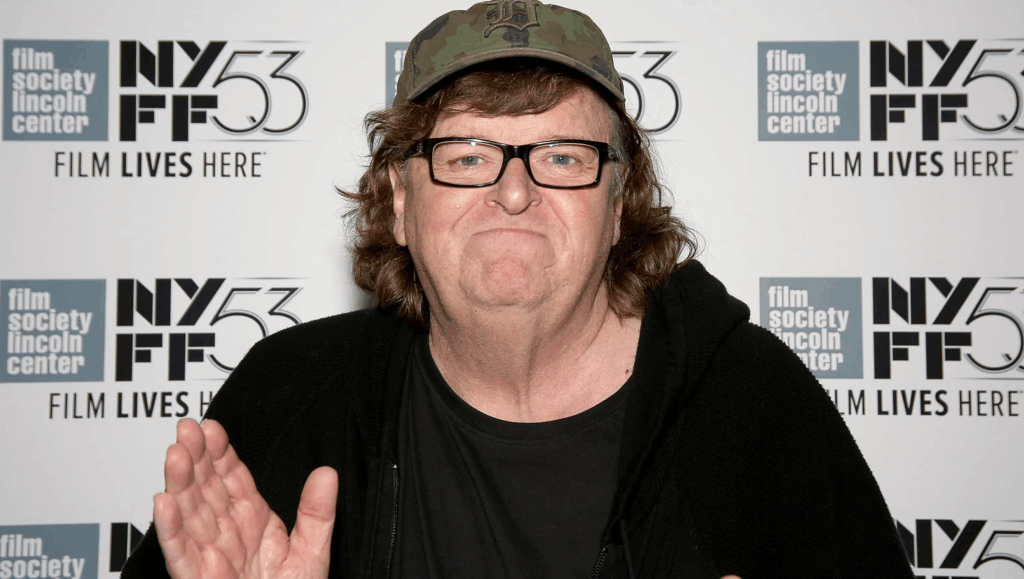 Michael Moore con cappellino e occhiali in posa durante un evento cinematografico, davanti a un backdrop con loghi del New York Film Festival.