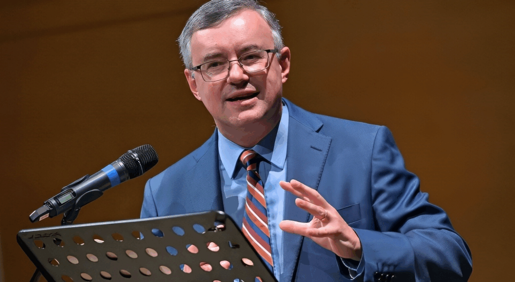 Relatore, prof. Barbero, in abito formale durante una conferenza storica, mentre spiega al pubblico temi legati al comunismo e alla teoria marxista.
