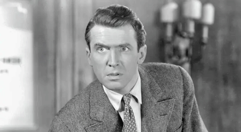 Scena in bianco e nero da un film d’epoca: uomo in abito elegante con sguardo teso, in primo piano.
