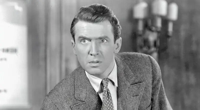 Scena in bianco e nero da un film d’epoca: uomo in abito elegante con sguardo teso, in primo piano.
