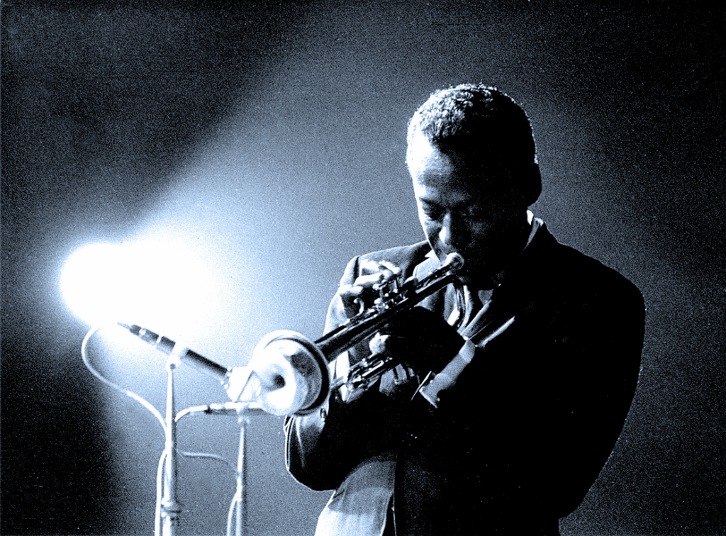 Miles Davis suona la tromba in un'atmosfera scura e intensa, simbolo del jazz moderno e dell'improvvisazione musicale.