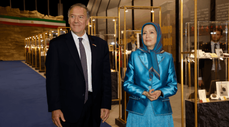 Incontro formale tra un ex leader politico statunitense e Maryam Rajavi, figura di spicco del MEK, in un contesto espositivo.