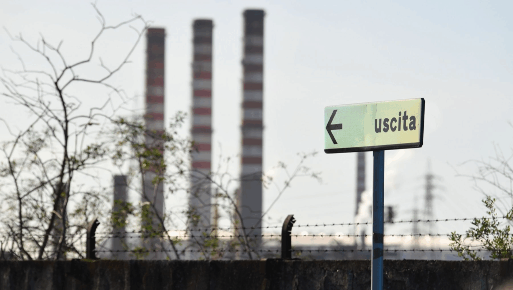 Ciminiere industriali e cartello "uscita", simbolo del declino manifatturiero italiano