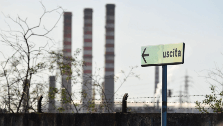 Ciminiere industriali e cartello "uscita", simbolo del declino manifatturiero italiano
