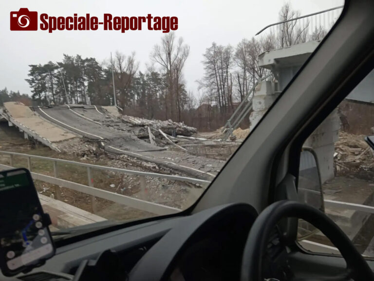 Vista dall'interno di un veicolo in Ucraina, con un ponte distrutto visibile oltre il parabrezza; immagine di un reportage di guerra.