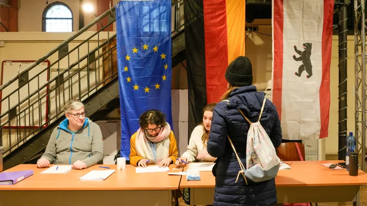 Una cittadina al seggio elettorale a Berlino durante le elezioni politiche 2024 in Germania, con bandiere dell’UE e del Land di Berlino sullo sfondo.
