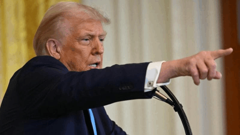 Donald Trump durante una conferenza stampa mentre indica con decisione, espressione determinata.