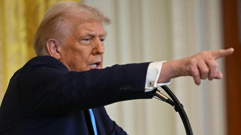 Donald Trump durante una conferenza stampa mentre indica con decisione, espressione determinata.