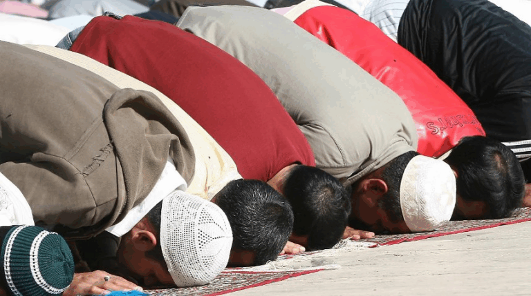 Fedeli musulmani in preghiera prostrati durante una funzione religiosa collettiva.