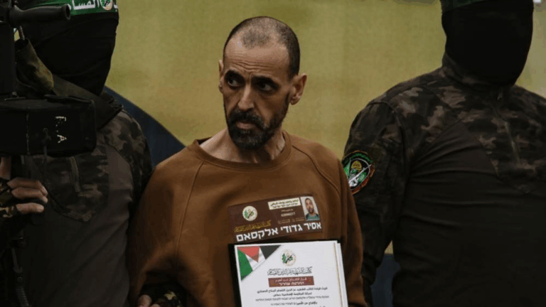 "Ostaggi israeliani liberati da Hamas: uomo visibilmente denutrito sorvegliato da miliziani mascherati durante la liberazione a Gaza."