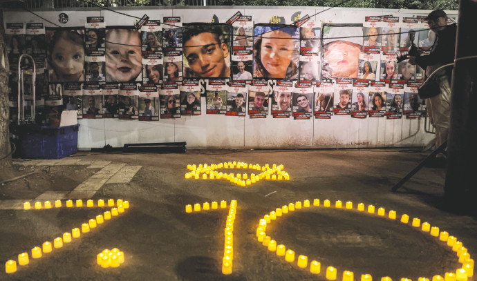 Vigilanza commemorativa con candele disposte a formare "7.10" e volti delle vittime sullo sfondo, in memoria degli attacchi del 7 ottobre.