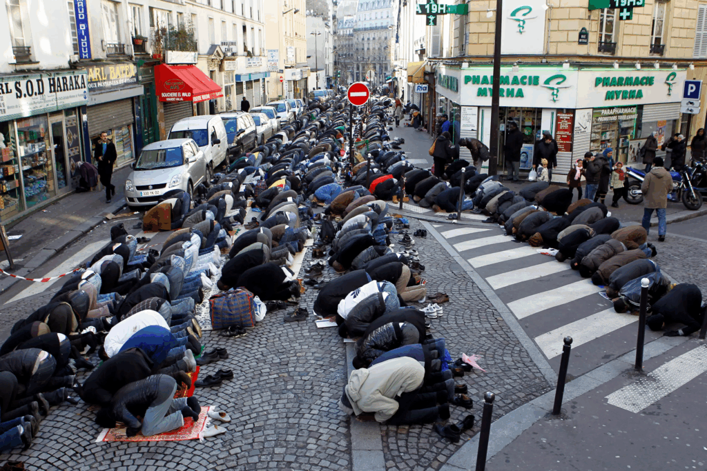 Fedeli musulmani pregano in strada durante la preghiera collettiva del venerdì in un quartiere urbano europeo.