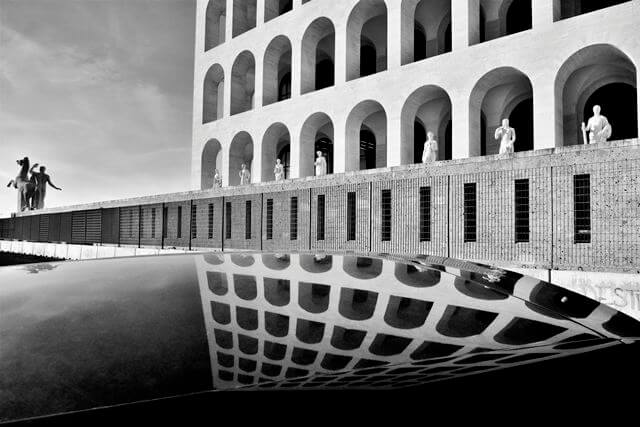 Palazzo della Civiltà Italiana all’EUR, simbolo dell’architettura razionalista a Roma, riflesso in una superficie d'acqua.