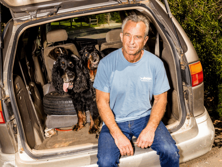 Robert Kennedy Jr. seduto sul retro di un’auto con due cani, in un contesto informale all’aperto