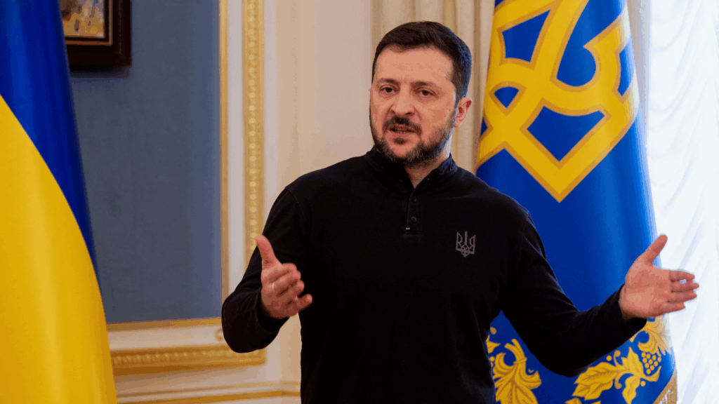 Presidente ucraino Volodymyr Zelensky in conferenza stampa, bandiere Ucraina e Tridente sullo sfondo – simbolo della resistenza contro l’invasione russa