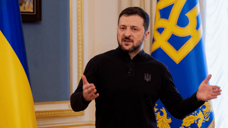 Presidente ucraino Volodymyr Zelensky in conferenza stampa, bandiere Ucraina e Tridente sullo sfondo – simbolo della resistenza contro l’invasione russa