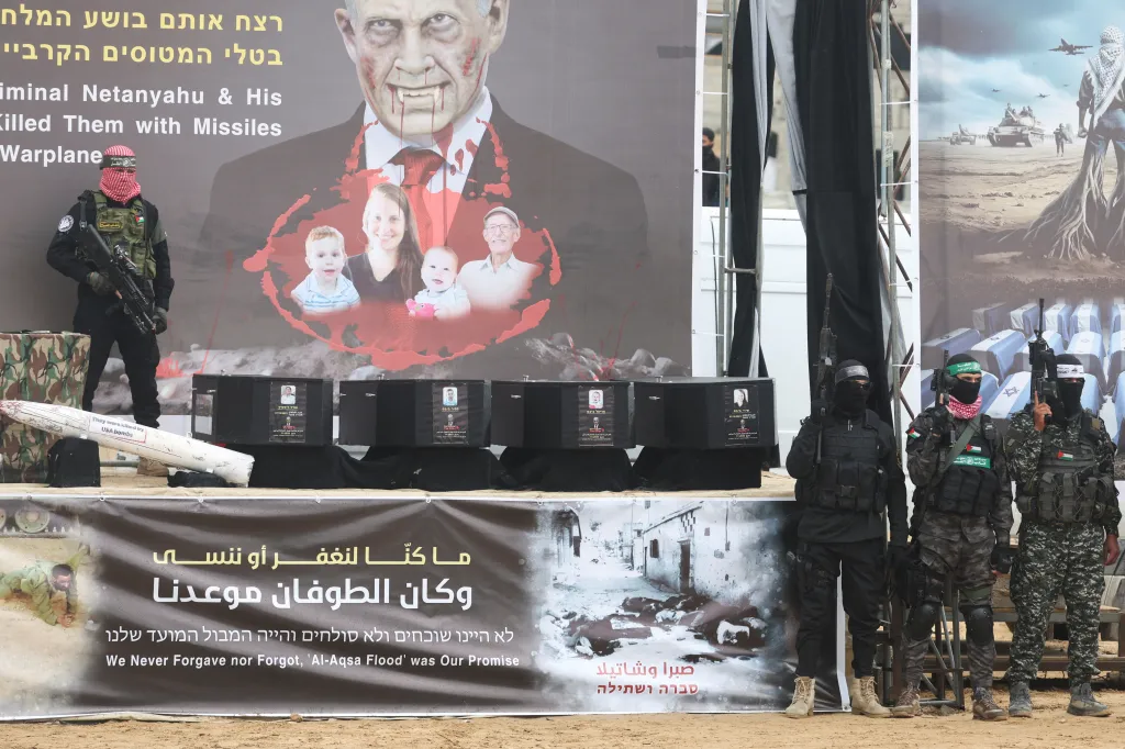 Miliziani di Hamas accanto a bare nere e a un poster propagandistico contro Israele durante una messa in scena pubblica a Gaza
