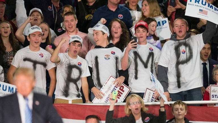 Giovani sostenitori di Donald Trump a un comizio, con magliette che formano la scritta 'TRUMP' tra la folla entusiasta