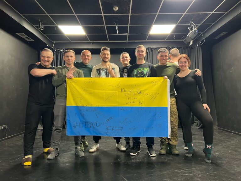 Gruppo di persone con bandiera ucraina in un ambiente chiuso, simbolo di sostegno alla resistenza e unità nazionale
