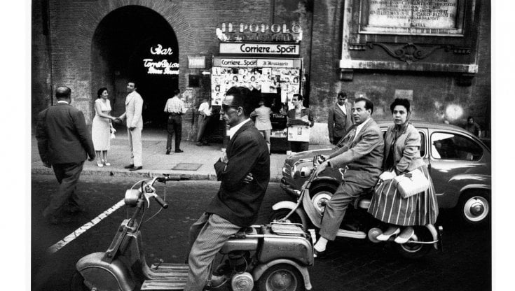 Scena di strada nella Roma degli anni '50, con passanti e scooter davanti a un cinema – atmosfera retrò in bianco e nero