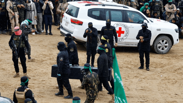 Miliziani di Hamas in parata con veicolo Croce Rossa sullo sfondo: simbolo delle ambiguità nel conflitto israelo-palestinese.