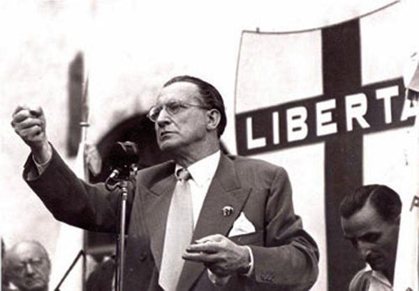 Alcide De Gasperi tiene un discorso pubblico davanti a un manifesto con la scritta "Libertà".