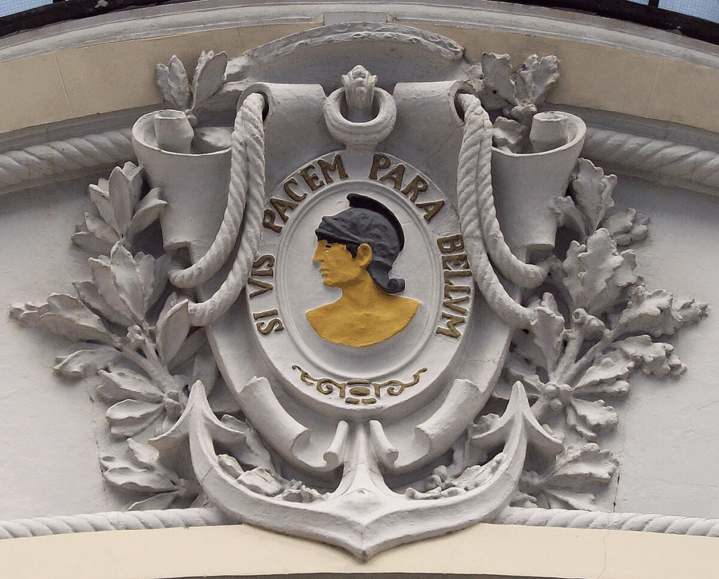 Bassorilievo con motto latino "Si vis pacem, para bellum" su edificio storico: simbolo della dottrina della deterrenza militare europea.