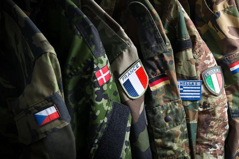 Uniformi militari di diversi paesi europei con bandiere nazionali cucite sulle maniche, simbolo della cooperazione nella difesa europea.