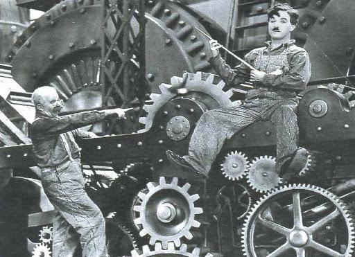 Charlie Chaplin tra gli ingranaggi di una macchina industriale nel film "Tempi moderni", simbolo della critica alla società industriale e tecnocratica.