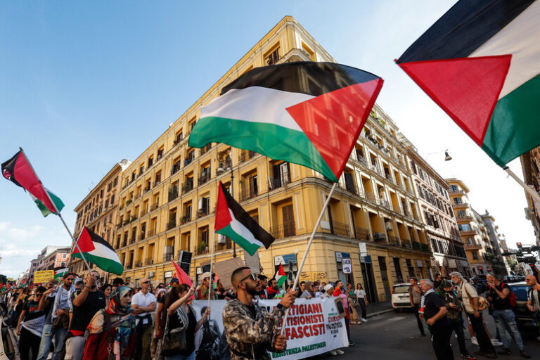 Manifestazione pro Palestina a Milano con bandiere palestinesi e striscioni contro Israele davanti a un palazzo storico.