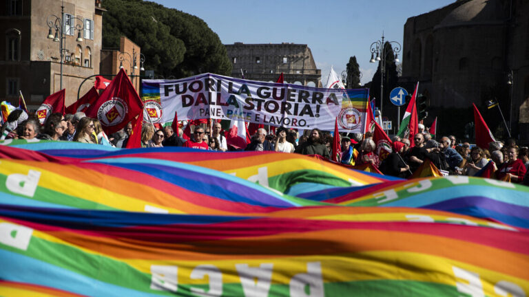 Manifestazione con bandiere arcobaleno della pace e striscioni contro la guerra durante un corteo pacifista in Italia.