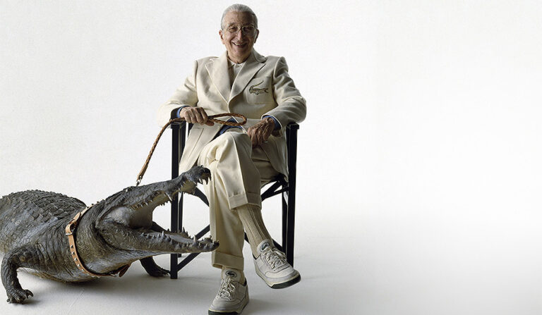 René Lacoste in completo chiaro seduto accanto a un grande coccodrillo al guinzaglio in un’evocazione simbolica del celebre logo del brand