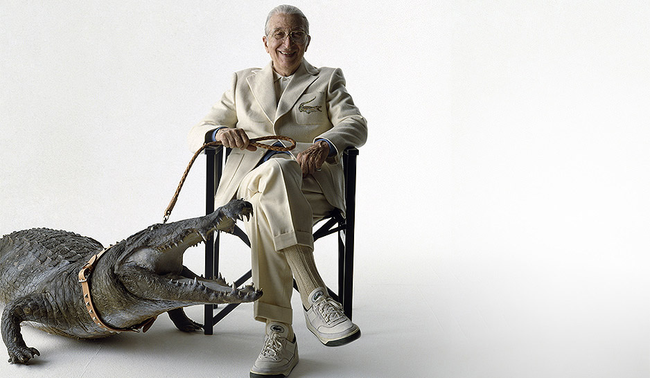 René Lacoste in completo chiaro seduto accanto a un grande coccodrillo al guinzaglio in un’evocazione simbolica del celebre logo del brand