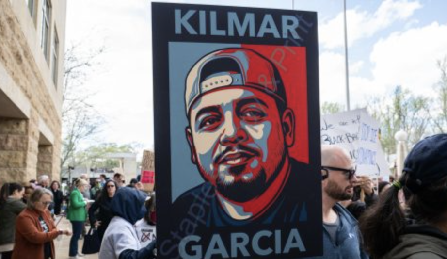 Manifestanti con cartello raffigurante Abrego Garcia durante una protesta, simbolo di abuso del potere democratico